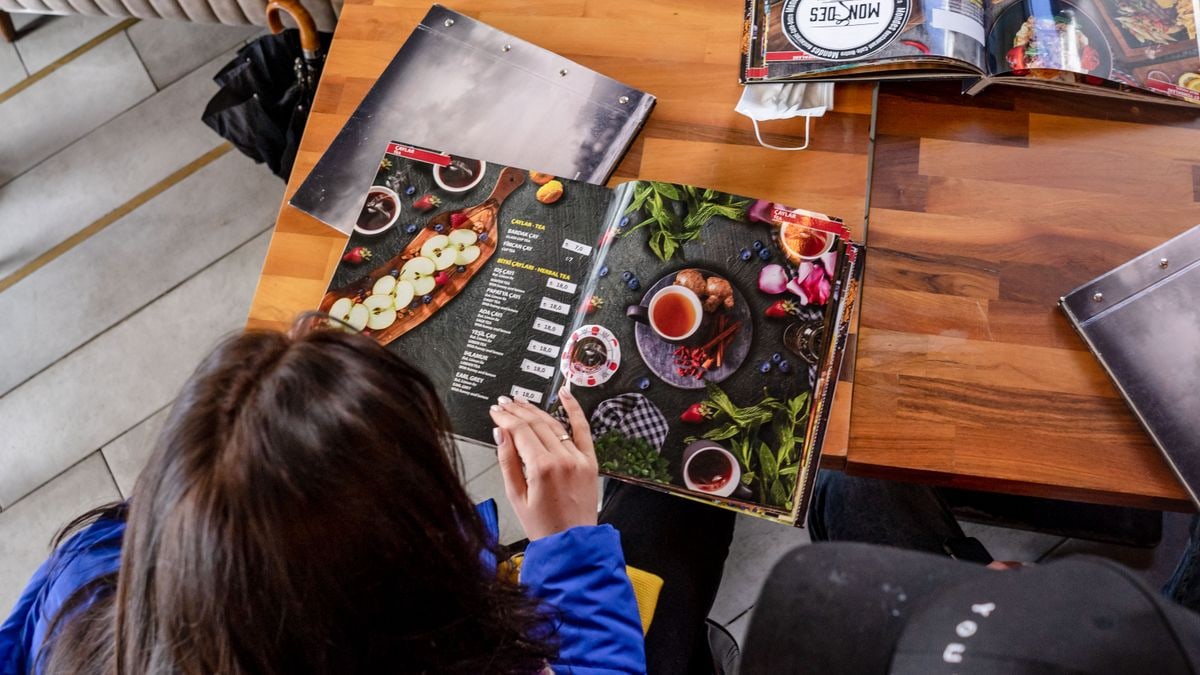 Two individuals explore food menus at a wooden table in a cozy café.